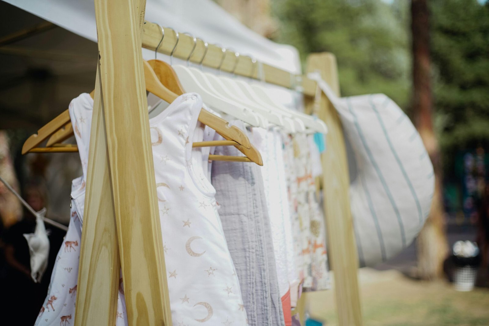 A variety of baby clothes hanging on wooden hangers at an outdoor market.