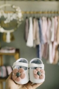 Cute white baby shoes with pink floral decoration held in hand, perfect for newborn fashion.