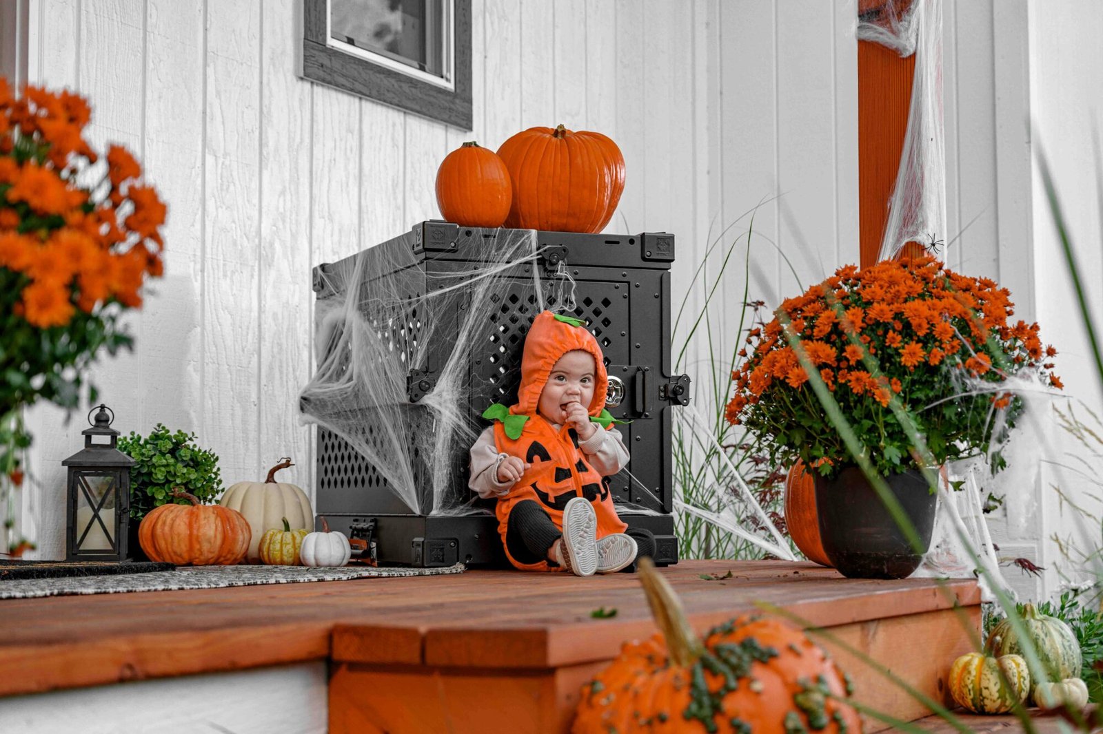 Baby in pumpkin costume on porch with Halloween decorations, holiday baby accessory factory.