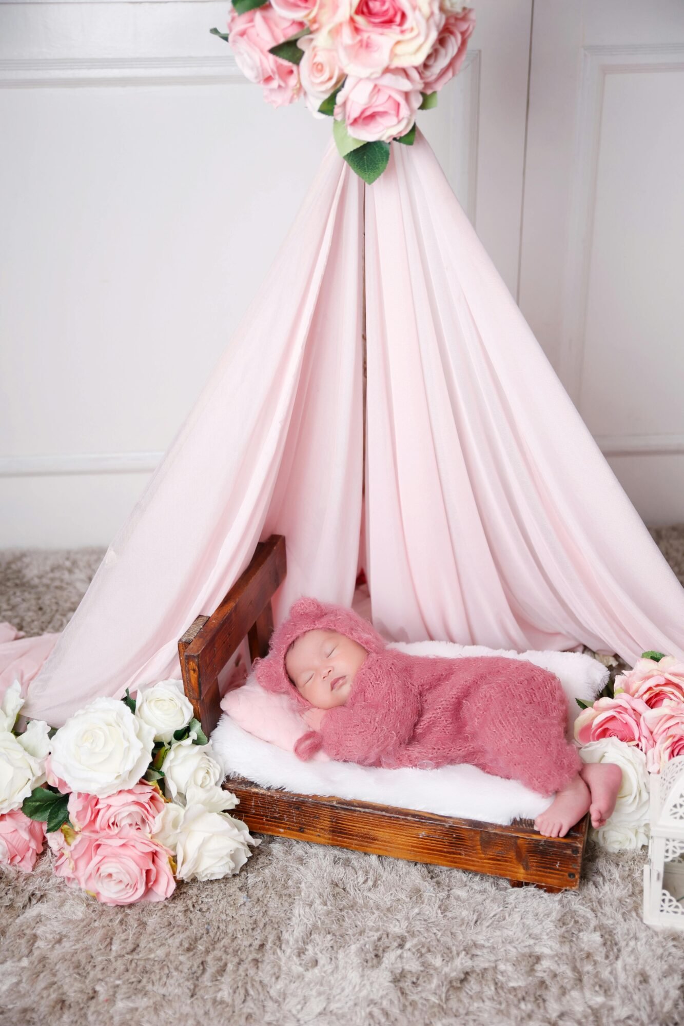Cute newborn baby girl in pink romper peacefully sleeping during a photoshoot with floral decor.