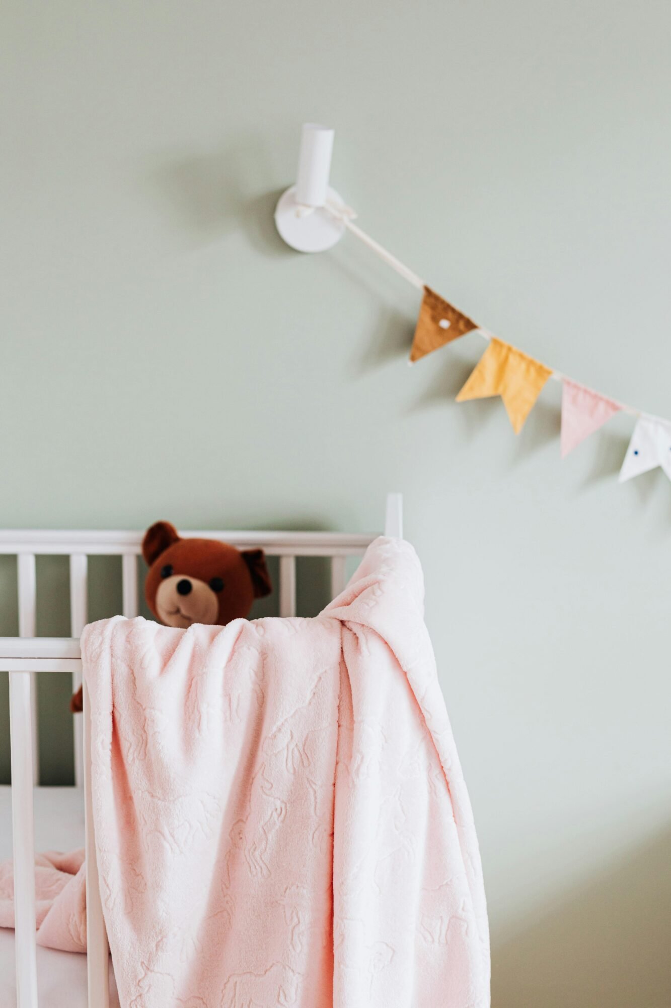 Cozy nursery corner featuring a cradle, teddy bear, and soft pink blanket, evoking warmth and comfort.