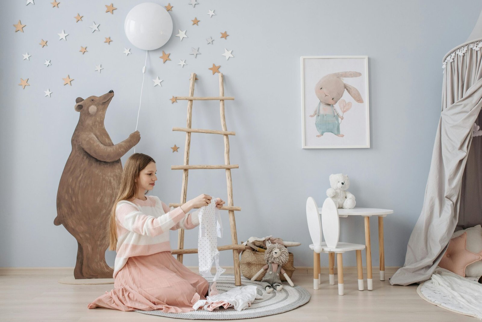 A woman folds baby clothes in a beautifully decorated nursery with a bear and star-themed design.