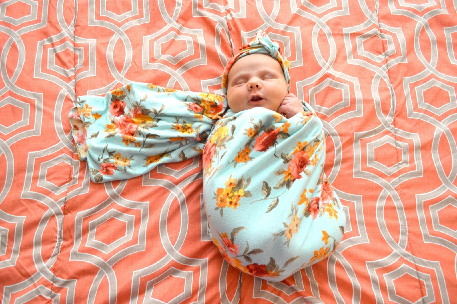 A peaceful baby wrapped in a vibrant floral blanket, lying on a patterned bedspread.
