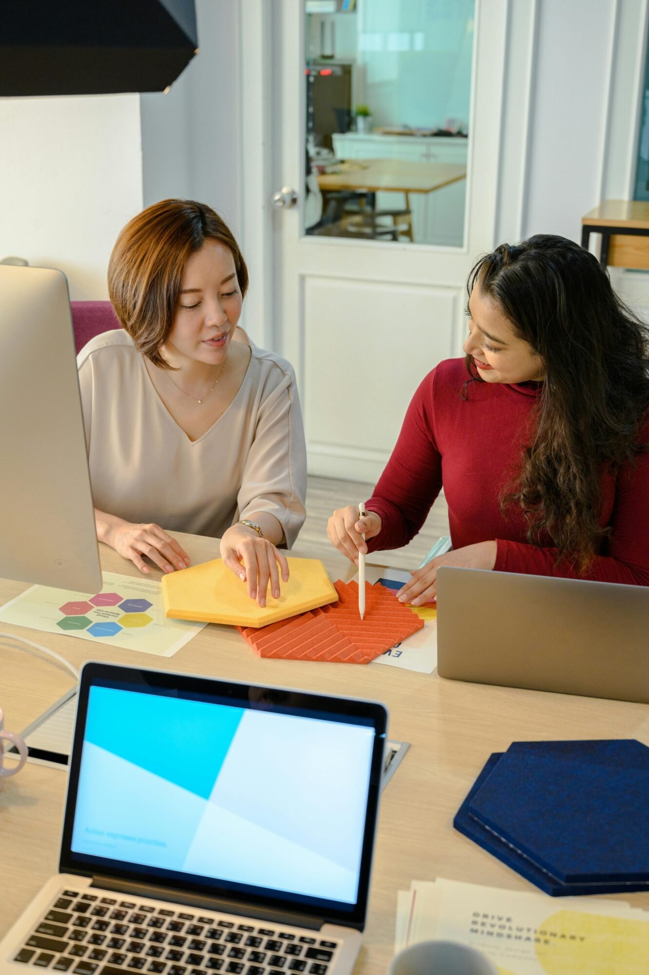 Two women collaborating on a creative project in a modern office environment.