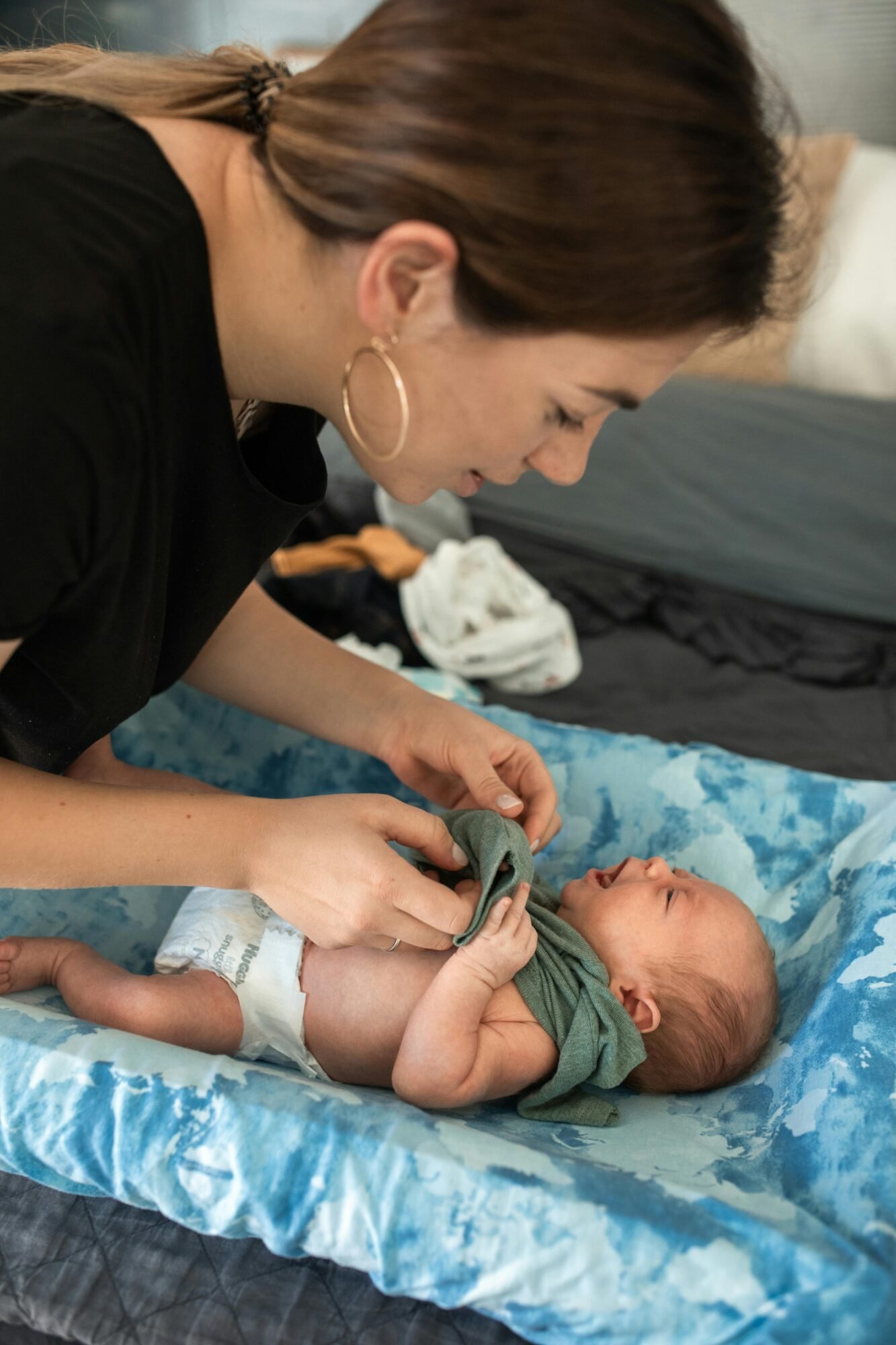 A loving mother gently dresses her newborn baby in cozy clothing indoors.